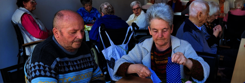 Eine Seniorin mit kurzen grauen Haaren bastelt aus Stoffresten einen Kranz